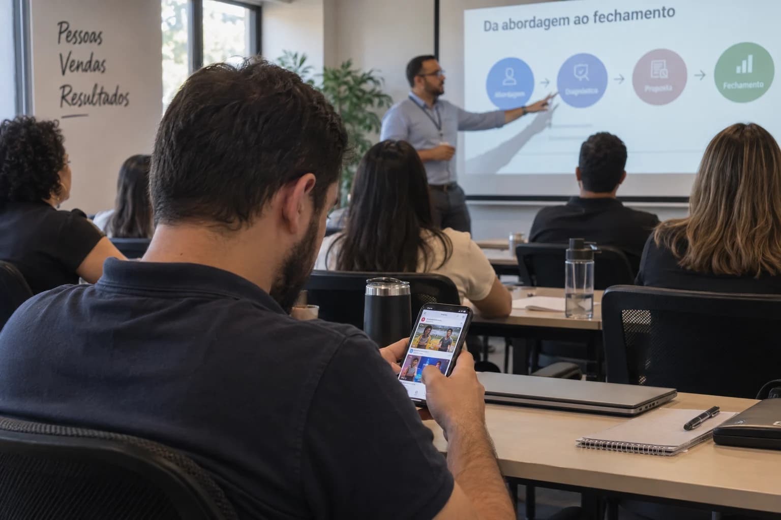 Participant scrolls social media on their phone while the instructor explains in the training room.